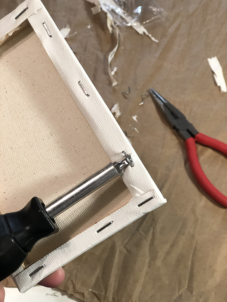 prying staples out of canvas with screwdriver and needle nose pliers
